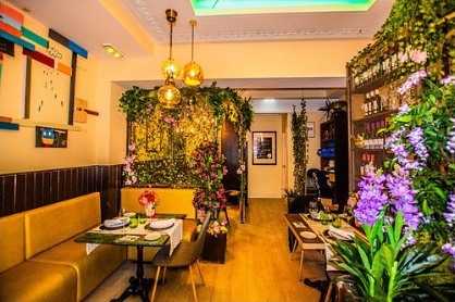 Comedor con mesas de madera, lámparas cálidas y una pared cubierta de plantas